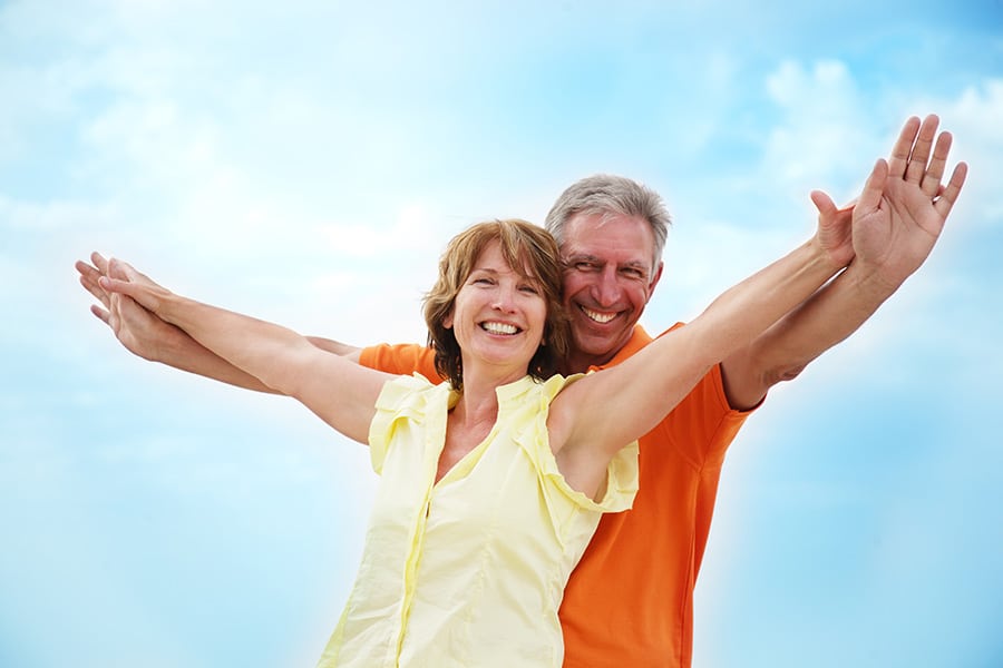 Mature couple with arms outstretched over a blue sky background